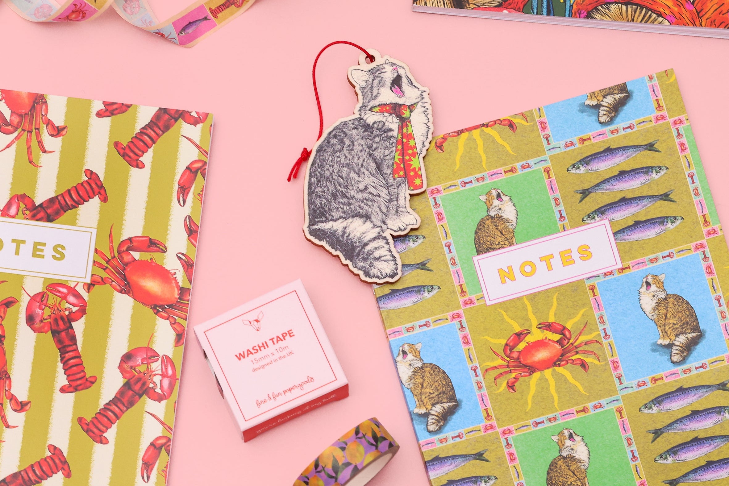 Colorful stationery items including a notebook, washi tape, and bookmarks on a pink background